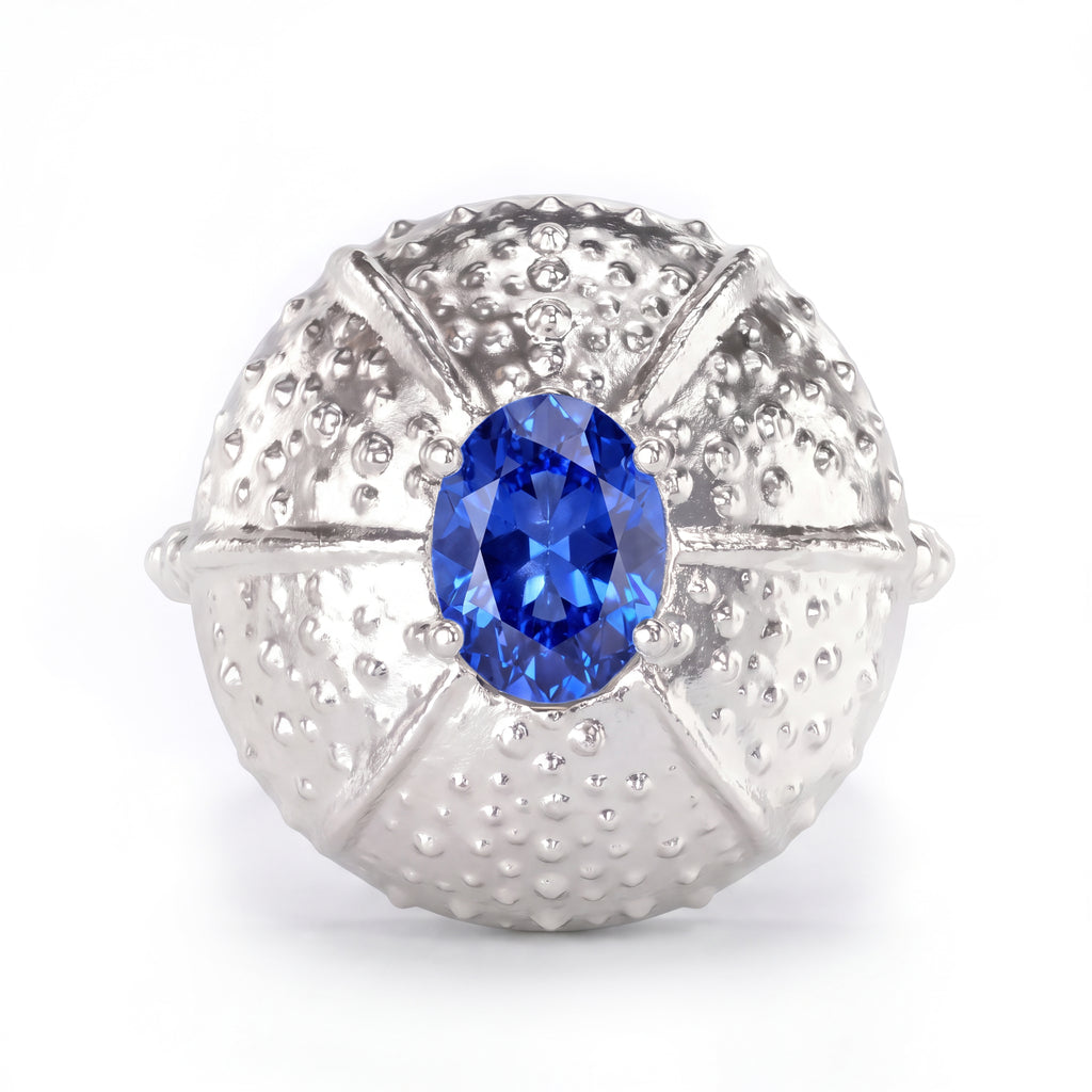 A white gold ring featuring a textured, sea urchin-inspired dome setting with a central blue sapphire, shown on a clean white background.