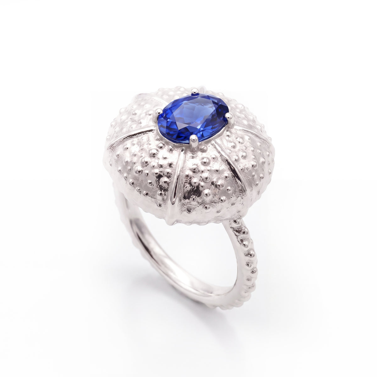 A white gold ring featuring a textured, sea urchin-inspired dome setting with a central blue sapphire, shown on a clean white background.