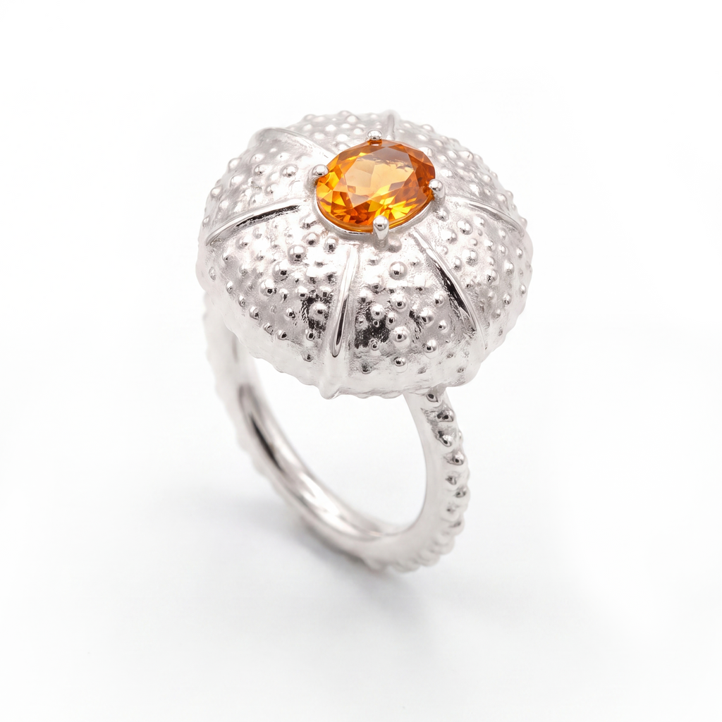 A white gold ring featuring a textured, sea urchin-inspired dome setting with a central oval orange sapphire, shown on a clean white background.