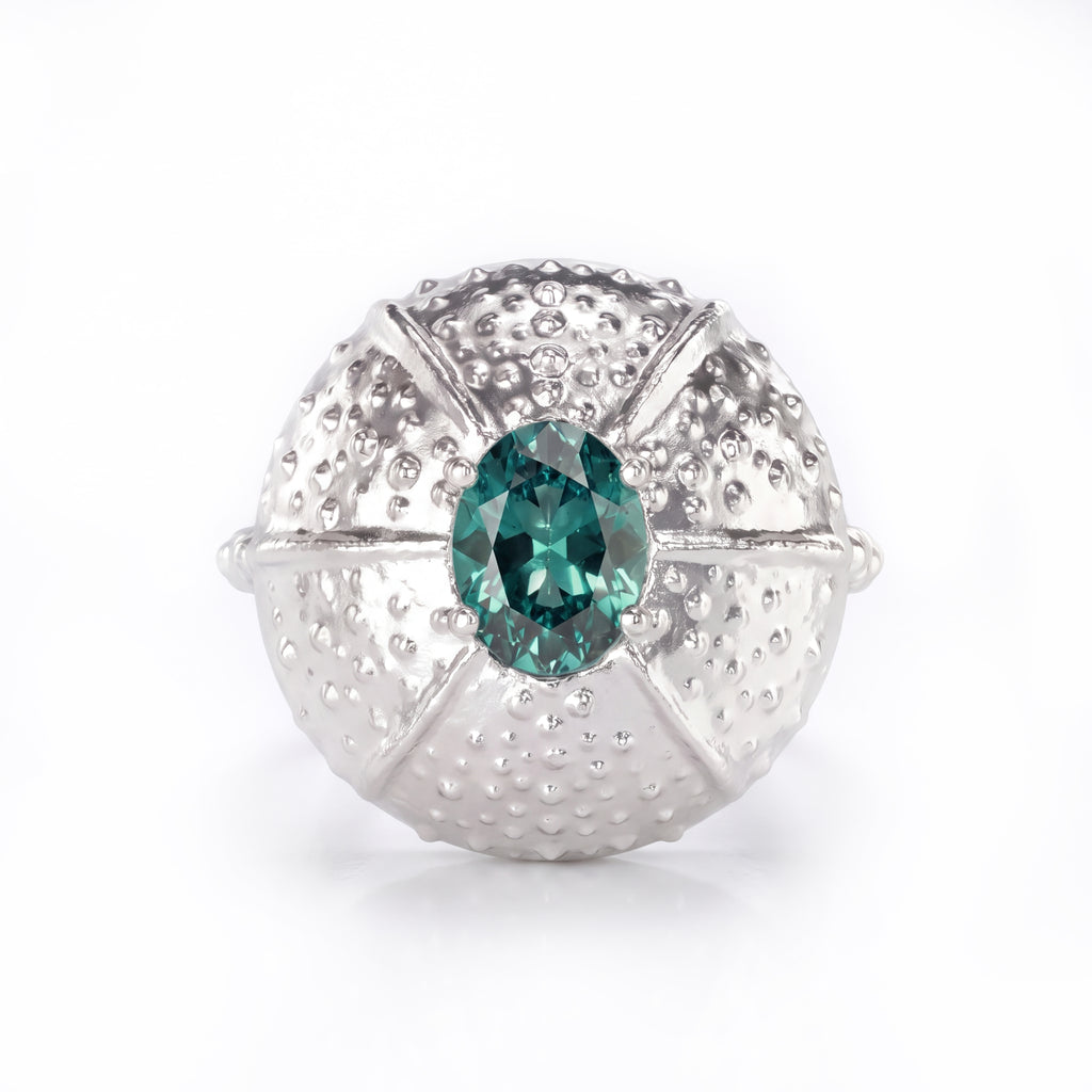 A white gold ring featuring a textured, sea urchin-inspired dome setting with a central teal sapphire, shown on a clean white background.