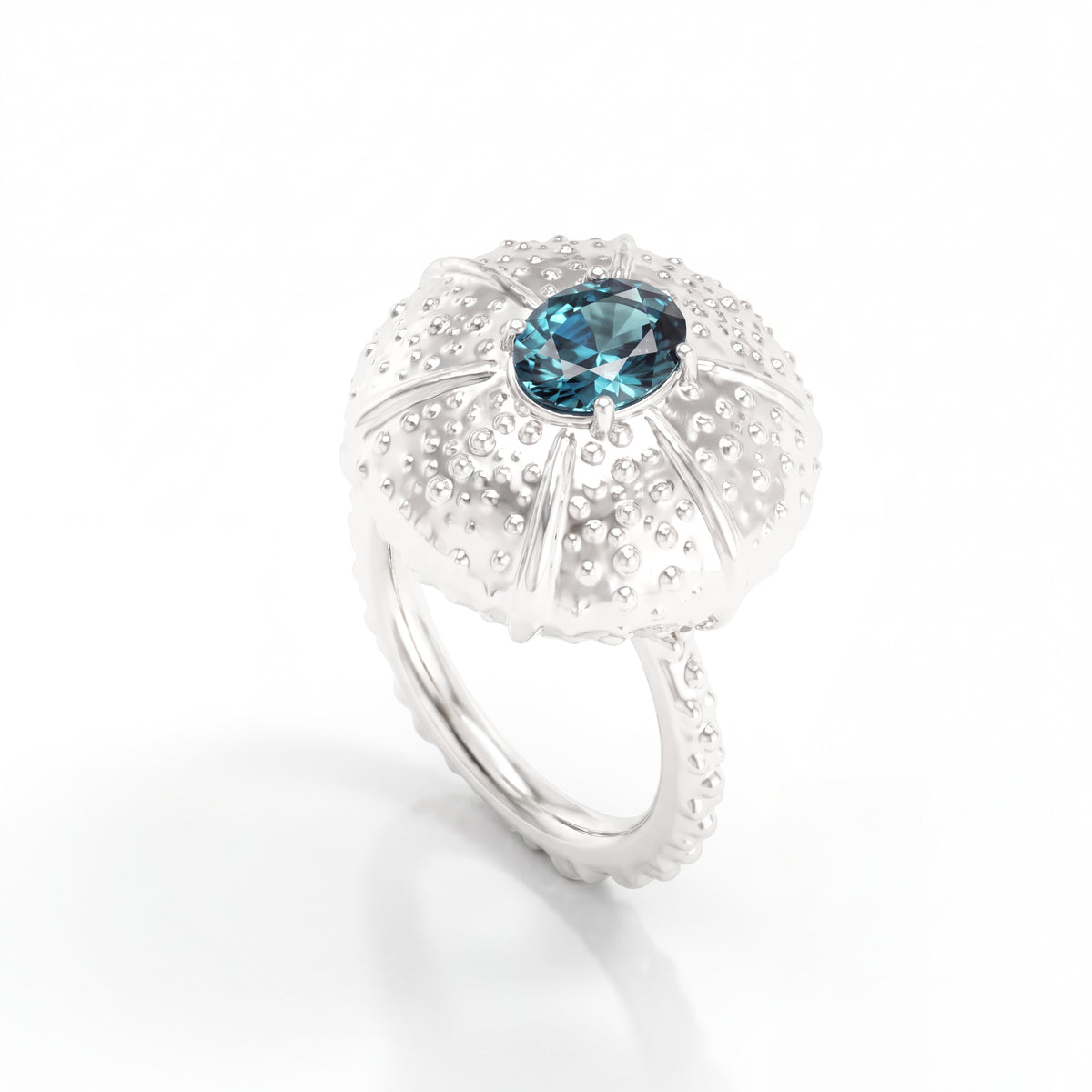 A white gold ring featuring a textured, sea urchin-inspired dome setting with a central oval teal saphire, shown on a clean white background.