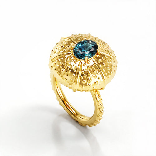 A yellow gold ring featuring a textured, sea urchin-inspired dome setting with a central oval teal sapphire, shown on a clean white background.